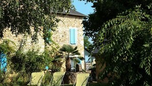 A stone building with a window, surrounded by greenery and a lawn with three chairs. - GÎTE DE LA COLLINE AUX FRAMBOISES (Oloron-Sainte-Marie)