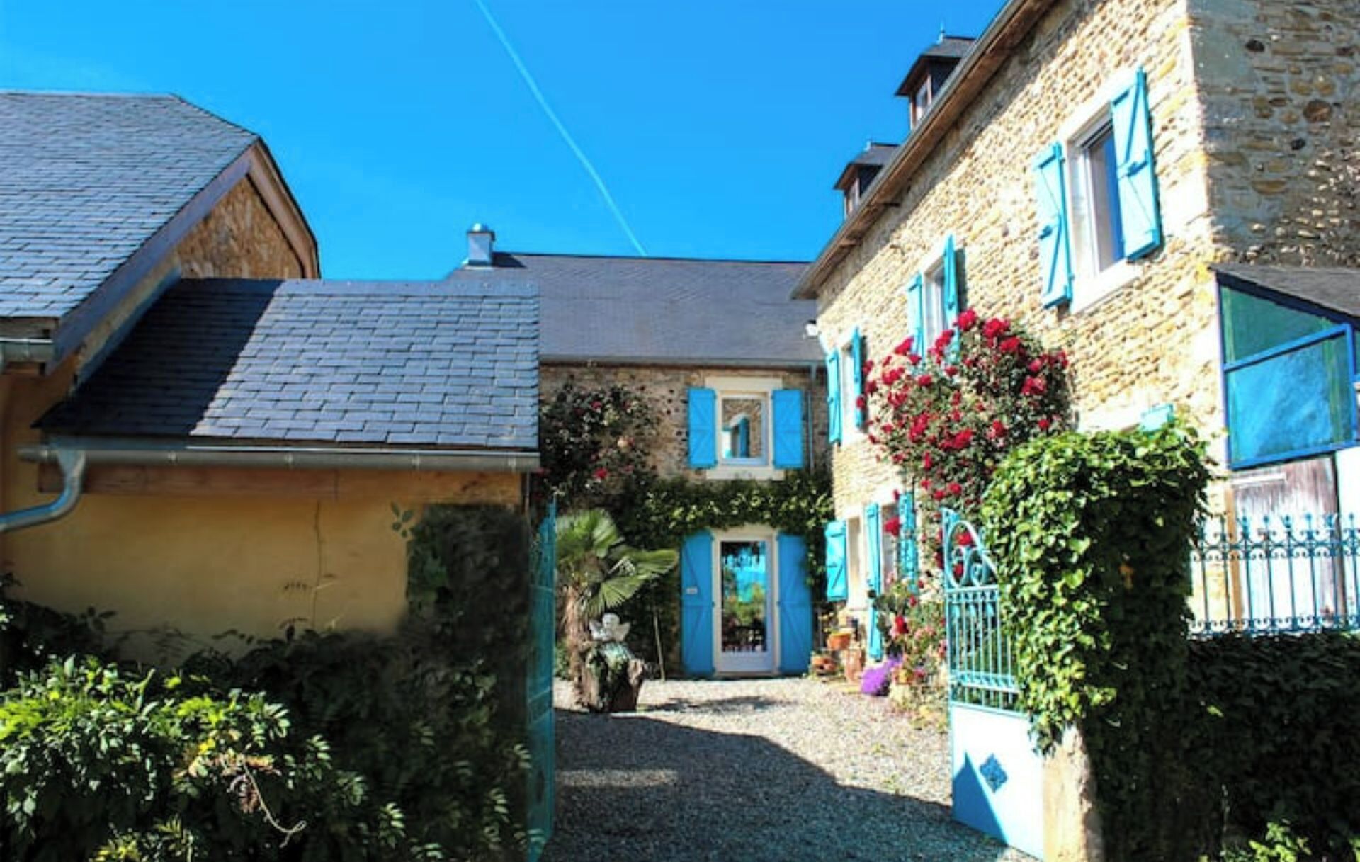 Un bâtiment traditionnel en pierre, avec une allée en gravier et un petit jardin agrémenté de fleurs.