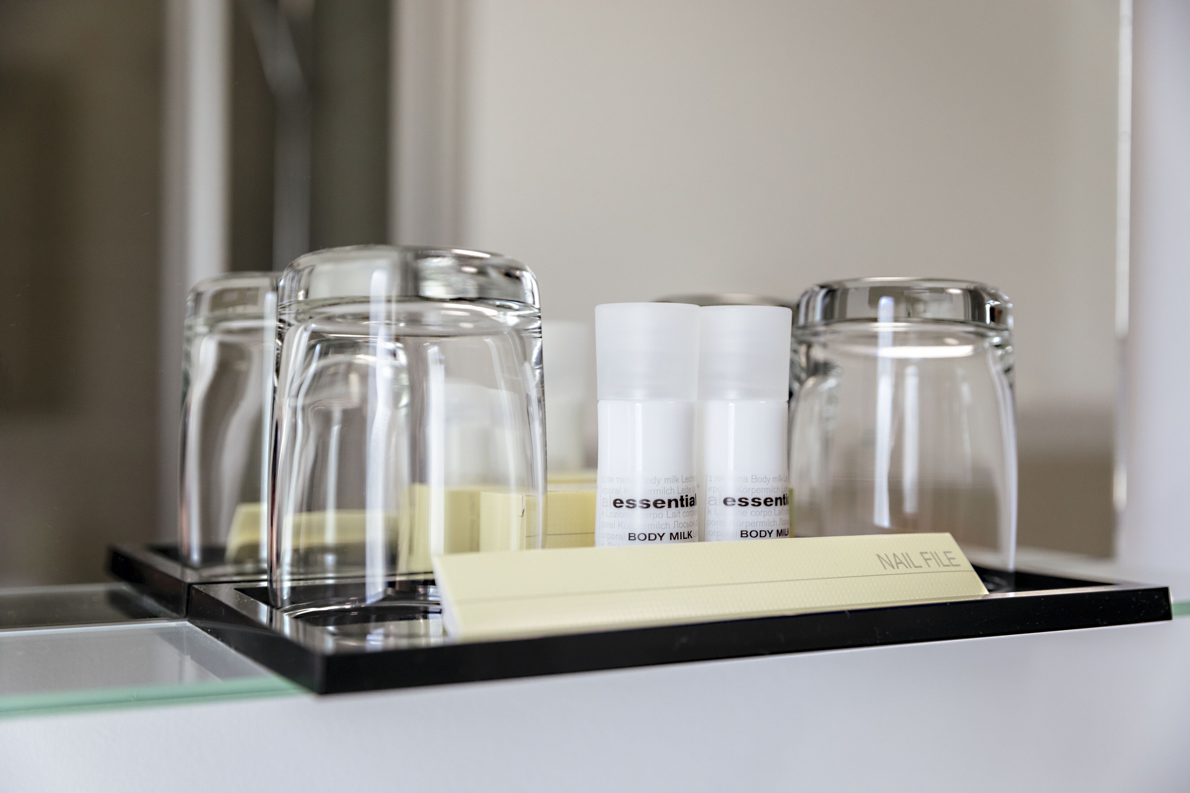 Een dienblad met drie heldere glazen flesjes, voorzien van de tekst 'essential body milk', en een klein kaartje met daarop 'Nail File'.