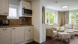 Eine moderne Küche mit Holzschränken, einer Mikrowelle und einer Kaffeemaschine. Es gibt eine Essecke mit einer Couch und Poufs.