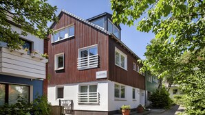 Ein modernes, zweistöckiges Gebäude mit einer Kombination aus weißem und dunklem Holzverkleidung, großen Fenstern und einem Schild, das es als Apartmenthaus der Insulaner kennzeichnet.