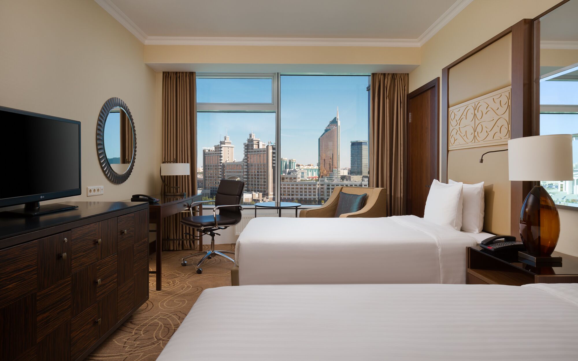 Habitación de hotel con dos camas, televisión, escritorio y vistas a la ciudad.