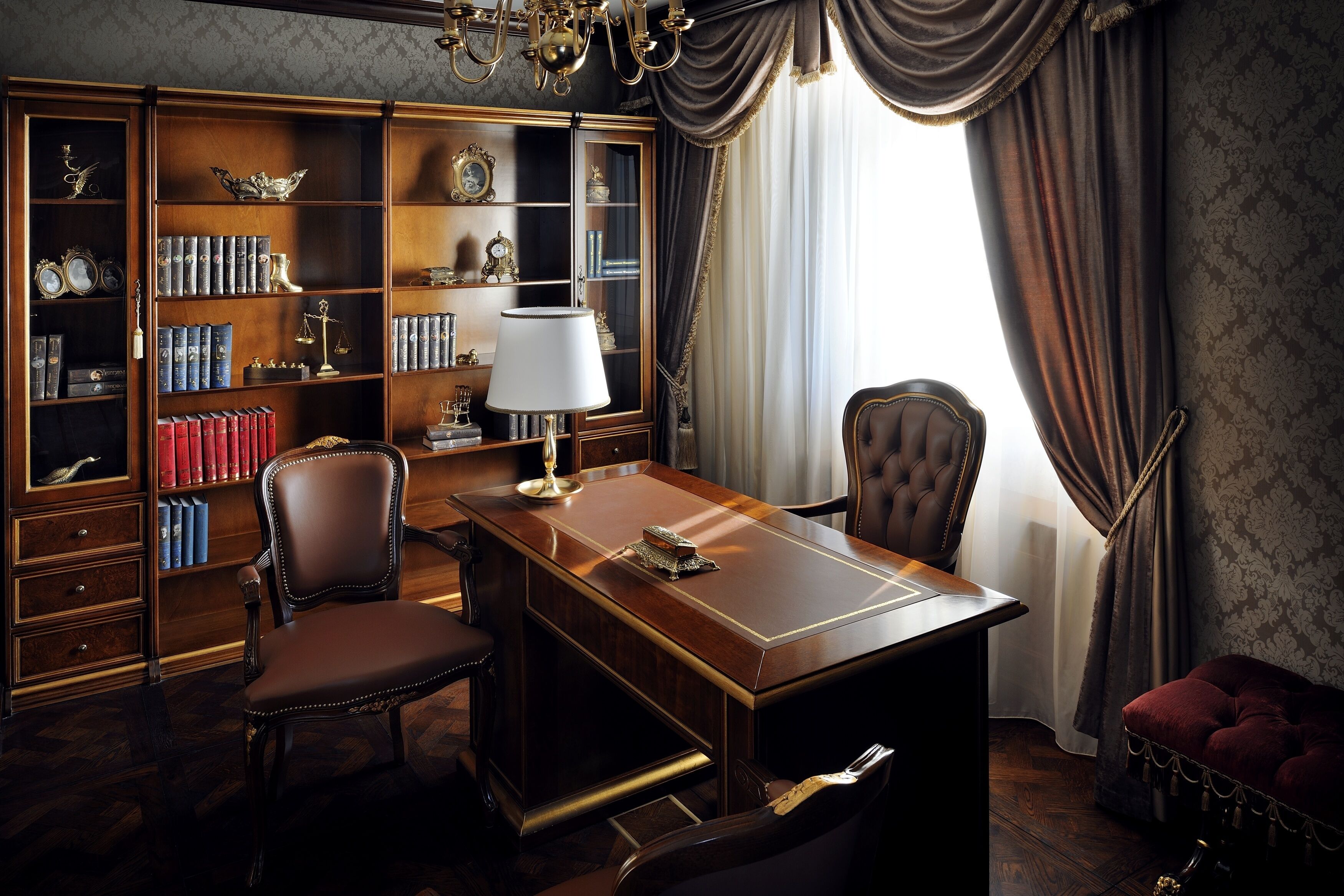 Una sala de estudio con un escritorio de madera, sillas de cuero, una estantería llena de libros y objetos decorativos, y un ventanal con cortinas.