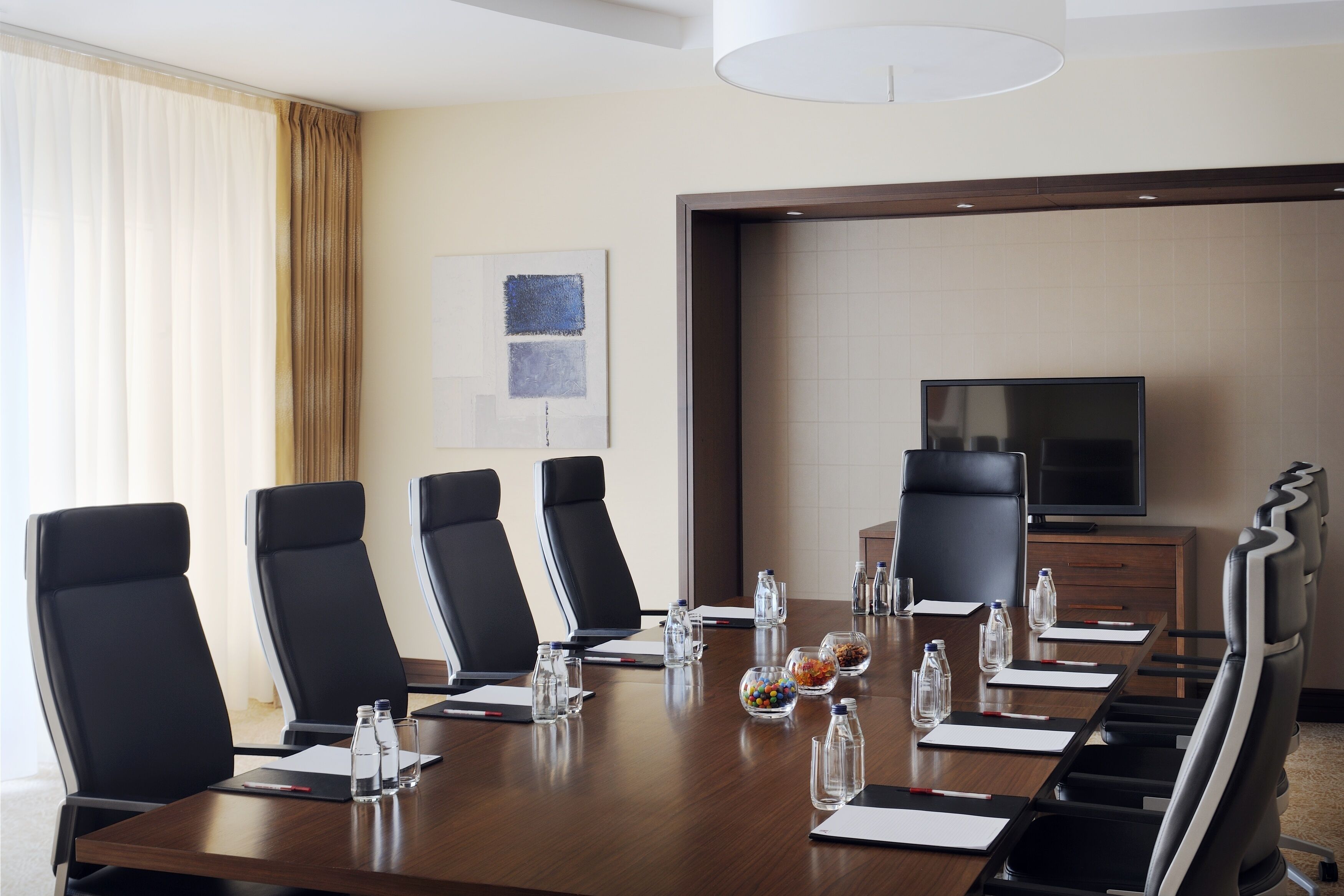 A conference room with a long table, six black chairs, a television, and a decorative wall piece.