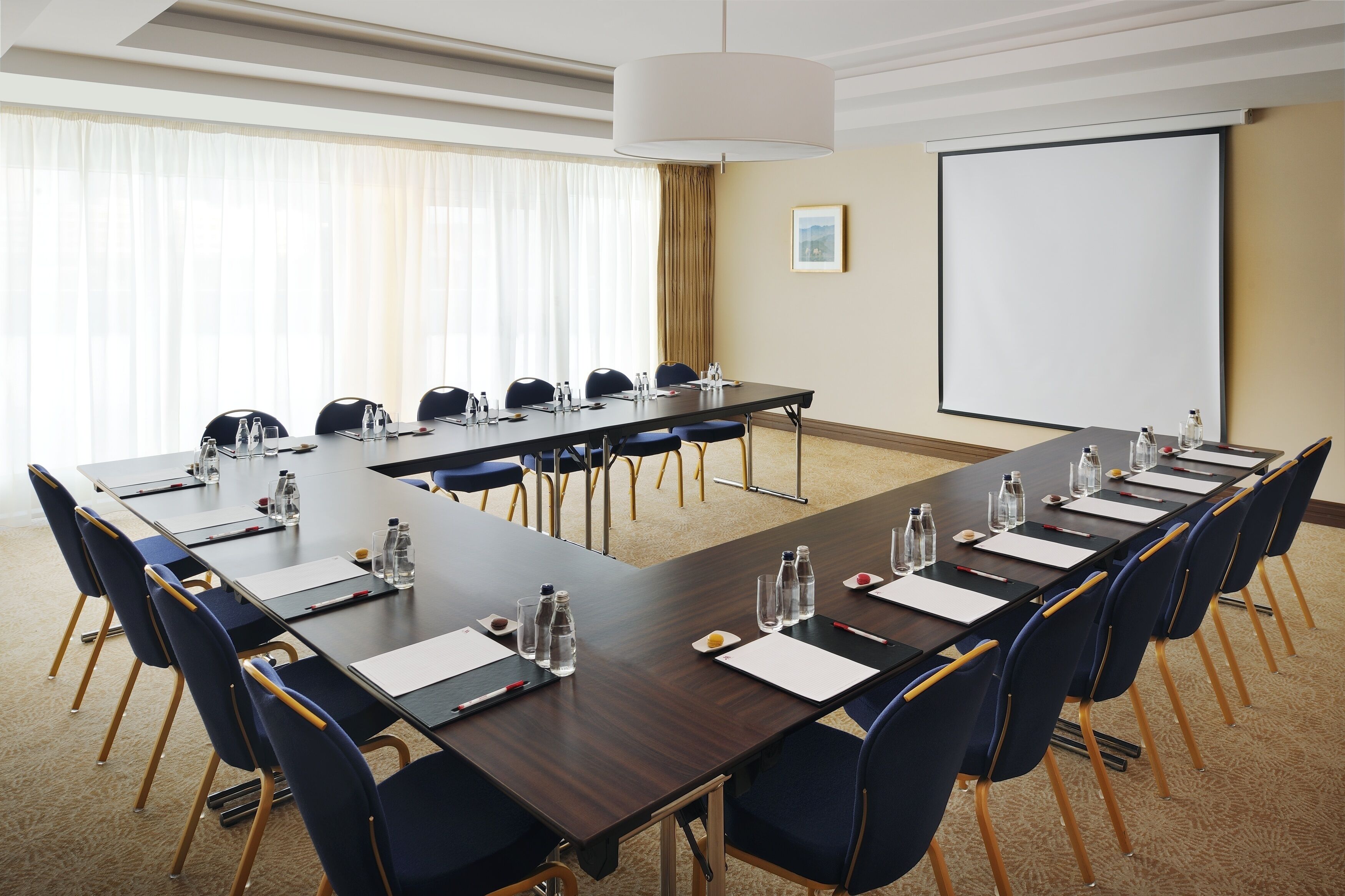 Ein Konferenzraum mit einem langen Tisch, Stühlen, Wasserflaschen und einer Projektionsleinwand.