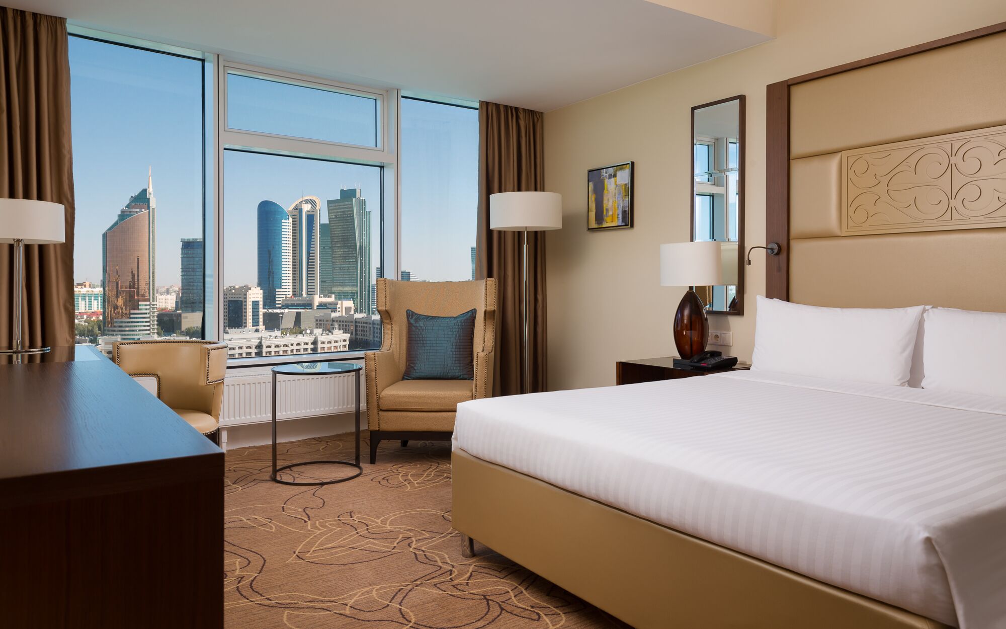 A hotel room with a large bed, a chair, a desk, and a view of the city skyline.