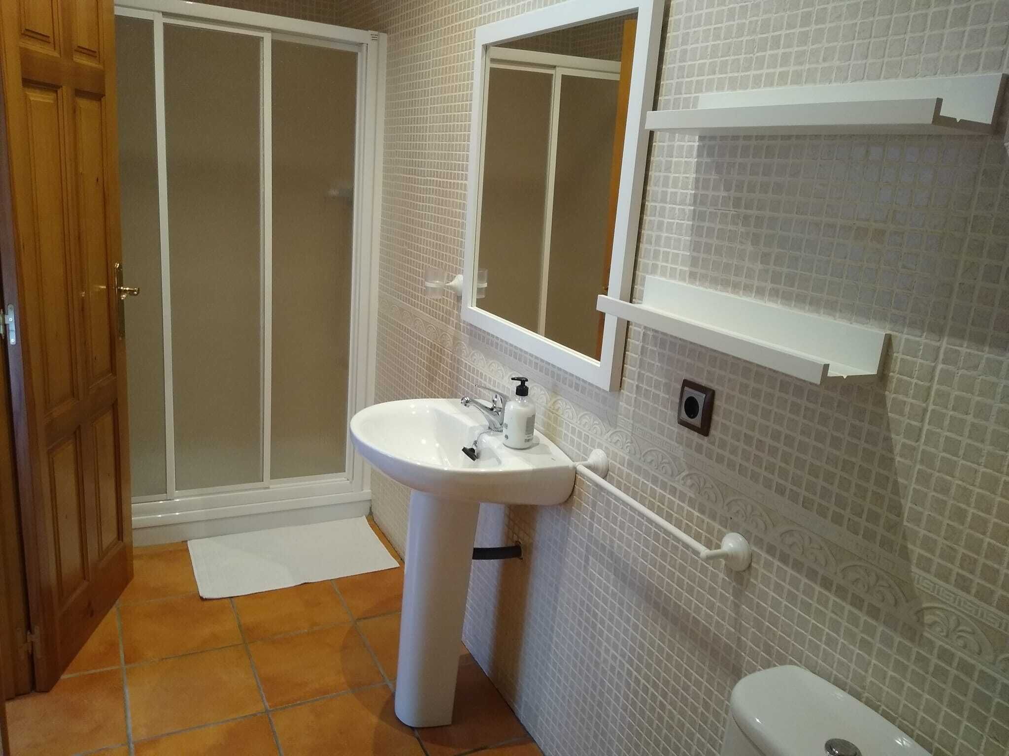 Un baño con lavamanos blanco, espejo, inodoro y zona de ducha.