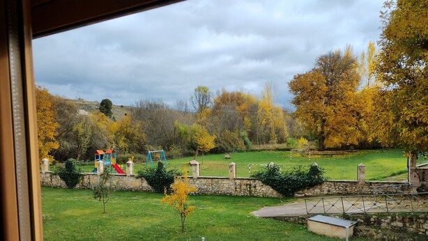 Vista de un parque con un patio de juegos, muros de piedra y árboles otoñales.
