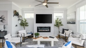 Una sala de estar moderna con chimenea, sofás blancos, una mesa de centro y un ventilador de techo.