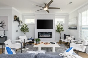 A modern living room with a fireplace, white sofas, a coffee table, and a ceiling fan.