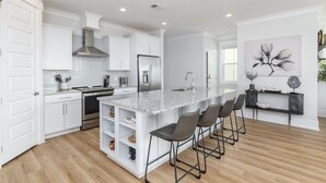 Una cocina moderna con armarios blancos, encimera de granito y una isla central con taburetes de bar.