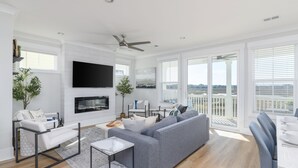 Una sala de estar moderna con un sofá gris, sillones blancos, un televisor de pantalla plana y un comedor con mesa y sillas.