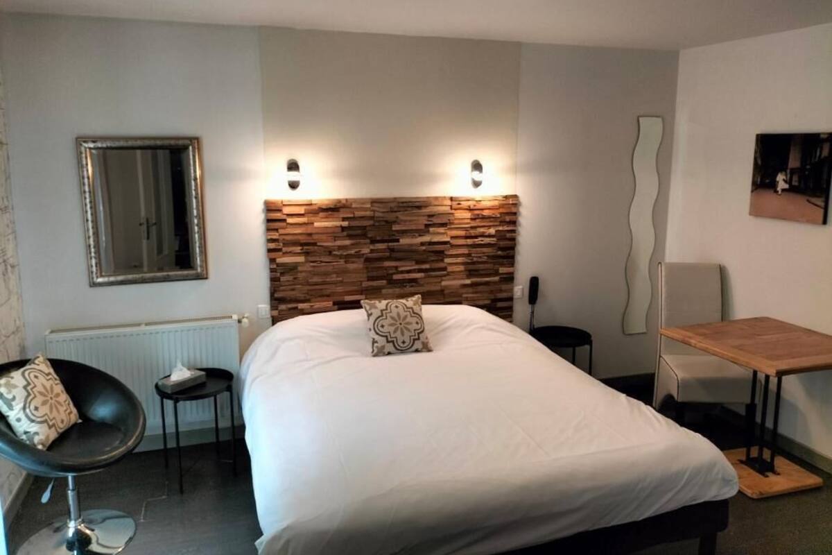 A hotel room with a large bed, a wooden headboard, a chair, a small table, and a mirror on the wall.