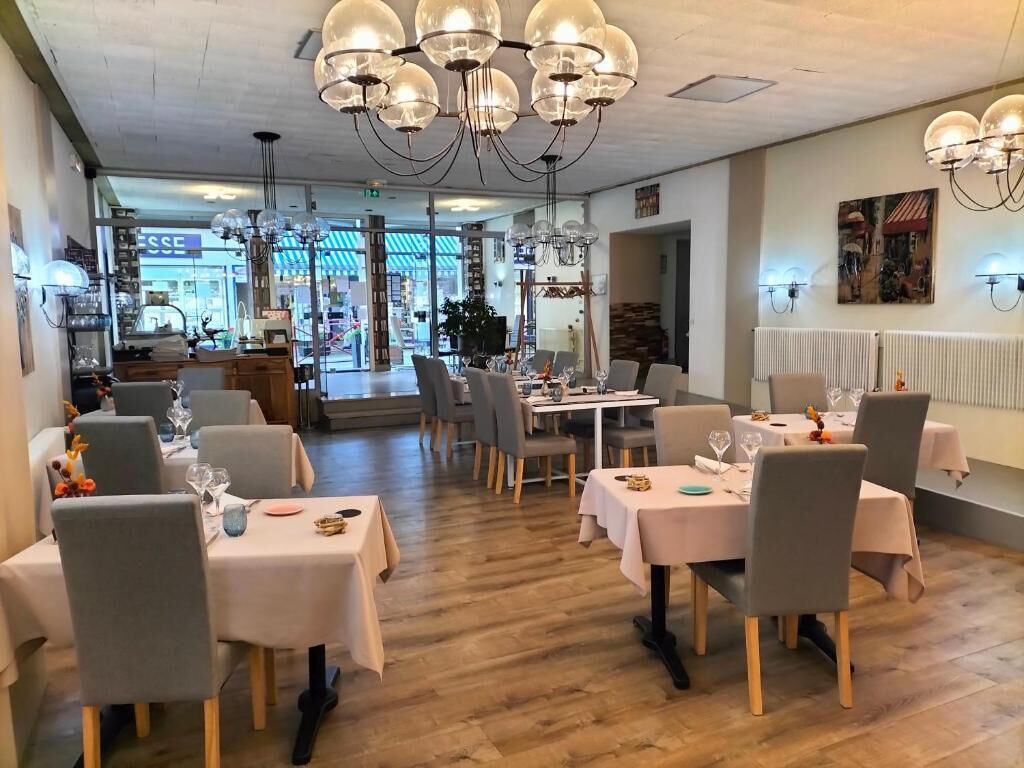 Un restaurant avec plusieurs tables dressées pour le service, un lustre et une vue sur la rue.