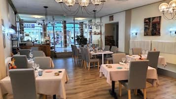 Un restaurant avec plusieurs tables dressées pour le service, un lustre et une vue sur la rue.