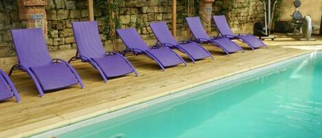A poolside area with purple lounge chairs aligned along the edge of a clear blue pool.