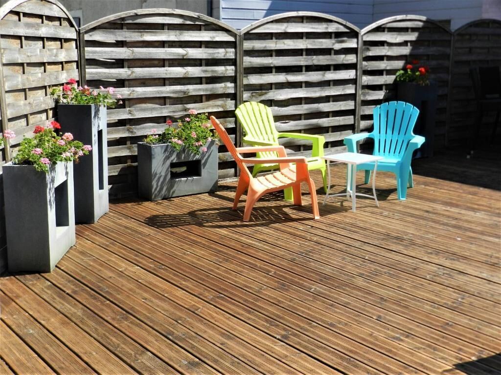 A wooden deck with colorful Adirondack chairs and planters with flowers.