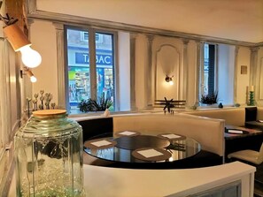 A modern interior with a round table, seating, and a view of a store through large windows. - HOTEL RESTAURANT HERARD  (Bourbonne-les-Bains)