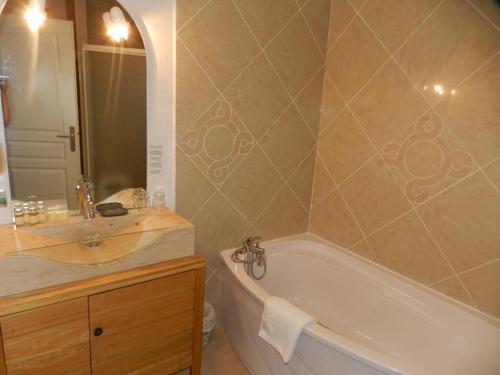 Een badkamer met een bad, een wastafel met spiegel en beige betegelde wanden.