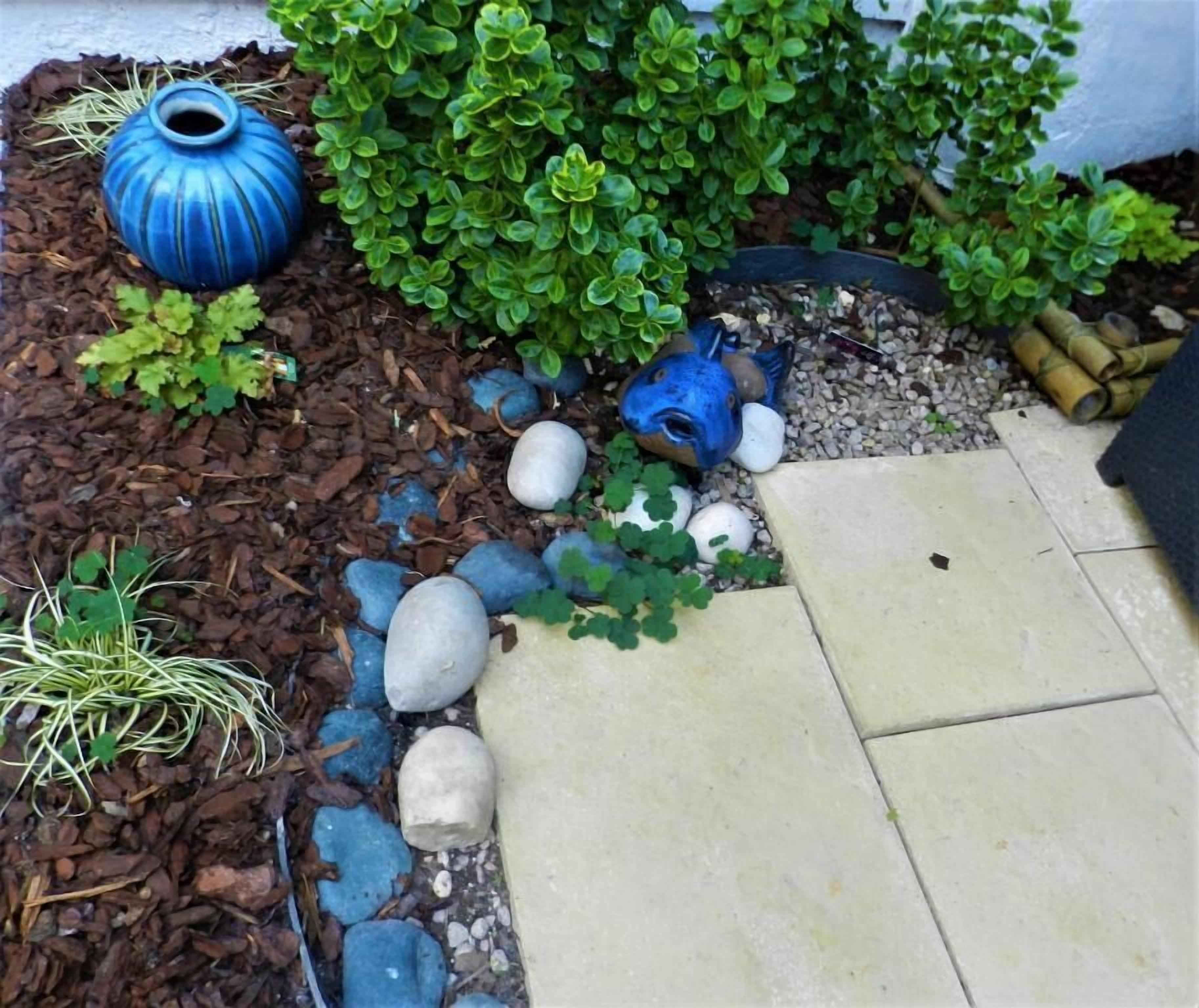 Un jardín con una maceta azul de cerámica, follaje verde y un sendero de piedra.