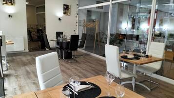 Un comedor moderno con mesas de madera y sillas blancas, separadores de vidrio y vista al espacio interior.