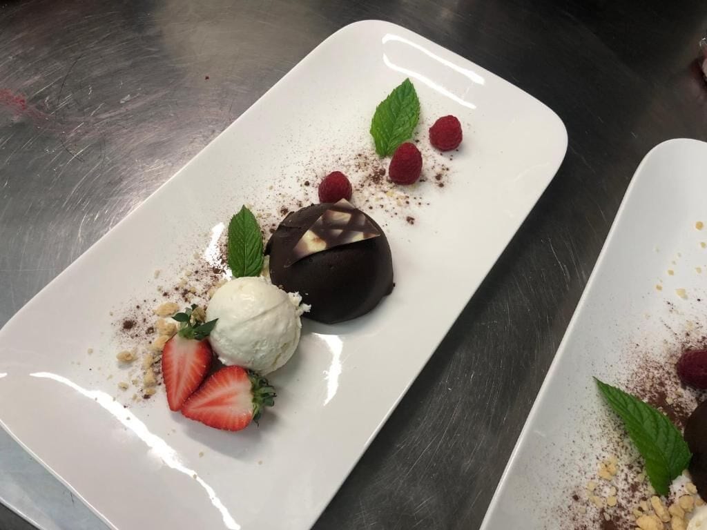 A dessert plate with chocolate, ice cream, strawberries, raspberries, and mint leaves.