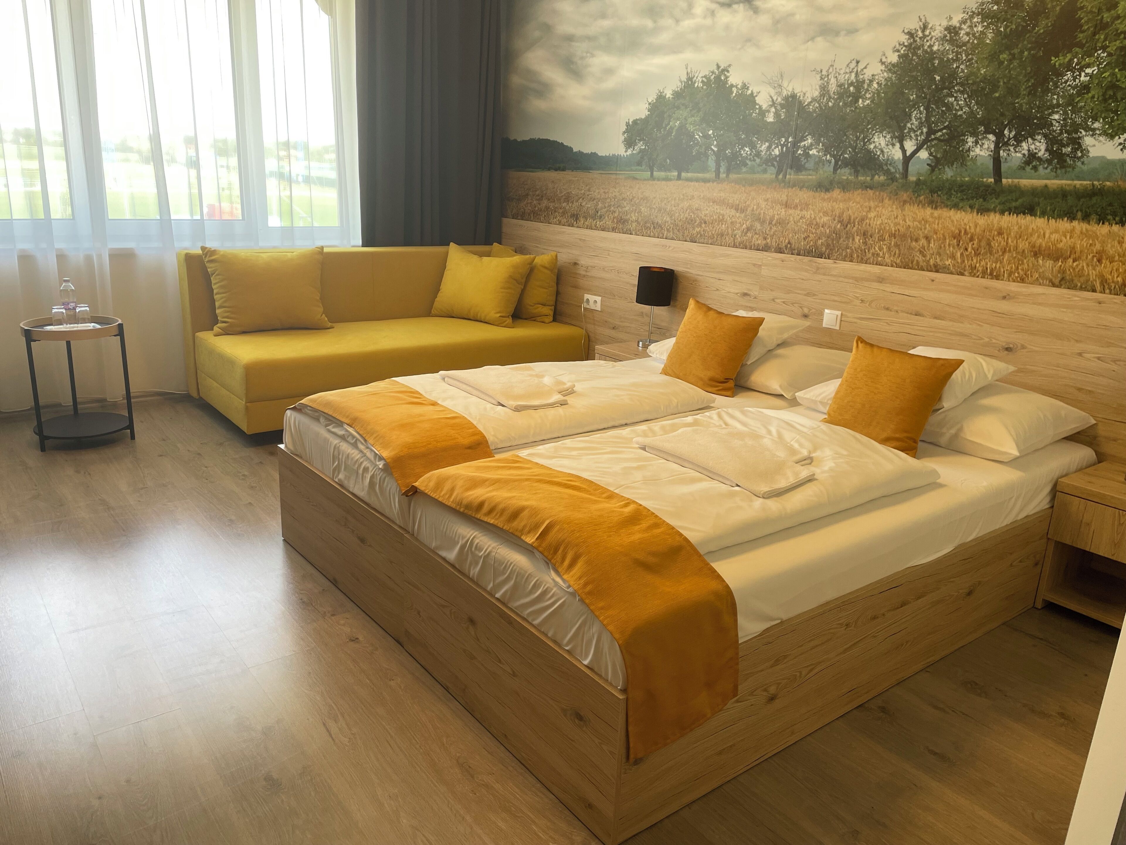 A bedroom with a large bed, a sofa, and a view of a field through a window.