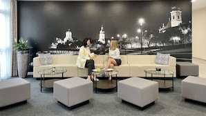 A modern lounge area with a large mural of a cityscape, a sofa, and several ottomans. - Gyirmót Sport&Wellness Hotel (Gyor)