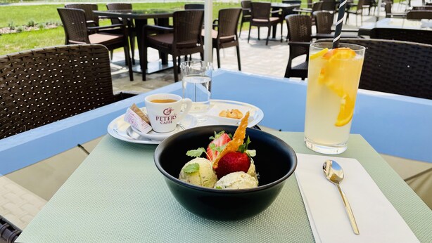 A table with a bowl of ice cream, a cup of coffee, a glass of iced tea, and a plate with cookies. - Gyirmót Sport&Wellness Hotel (Gyor)