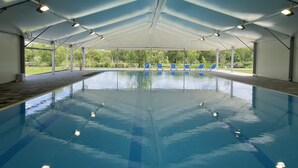 An indoor swimming pool with a covered roof, clear pool water, and several blue lounge chairs along the edge. - Gyirmót Sport&Wellness Hotel (Gyor)