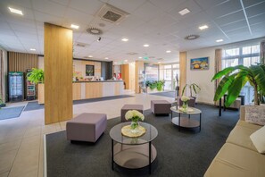 A modern lobby with a reception desk, seating areas, and a large window. - Gyirmót Sport&Wellness Hotel (Gyor)