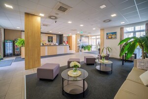 Um lobby moderno com balcão de recepção, áreas de estar e uma grande janela.