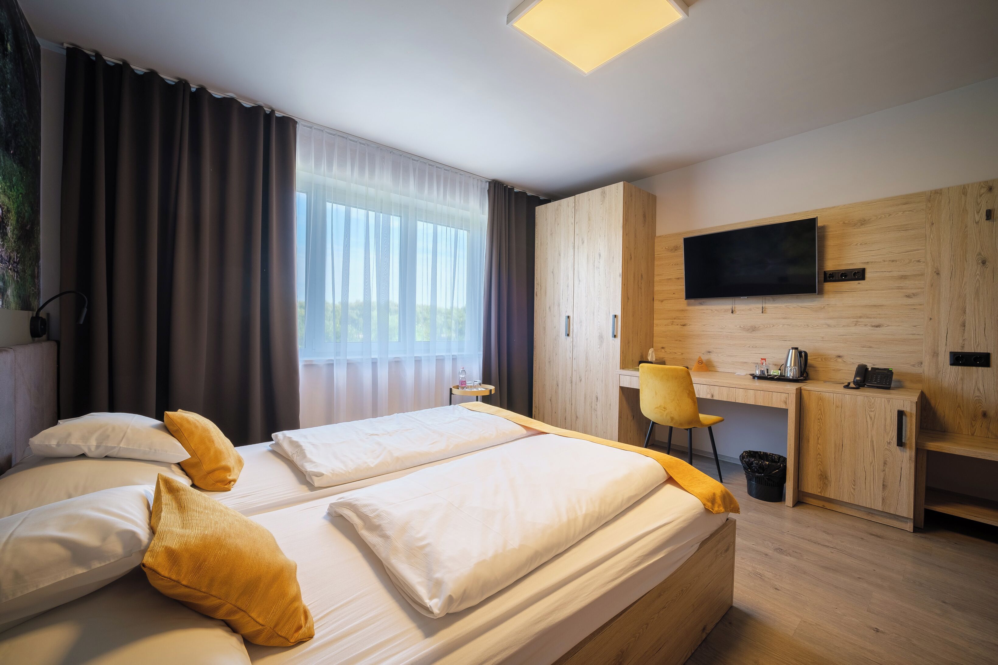 A hotel room with a bed, a desk, a chair, a TV, and a window with curtains.