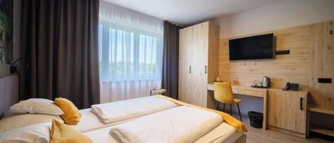 A hotel room with a bed, a desk, a chair, a TV, and a window with curtains.