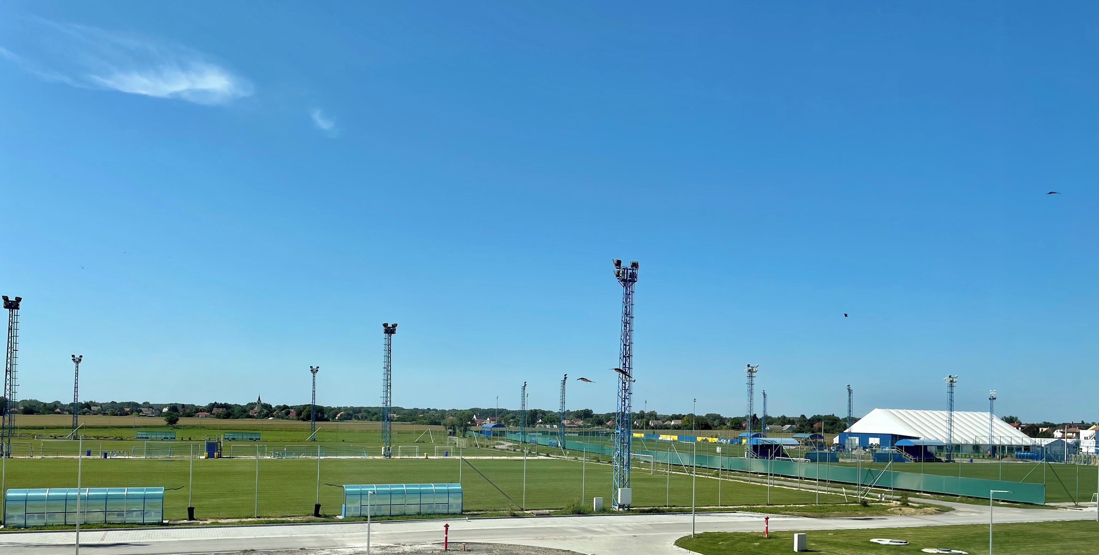 Um campo esportivo iluminado, com área de assentos coberta e uma grande tenda branca.