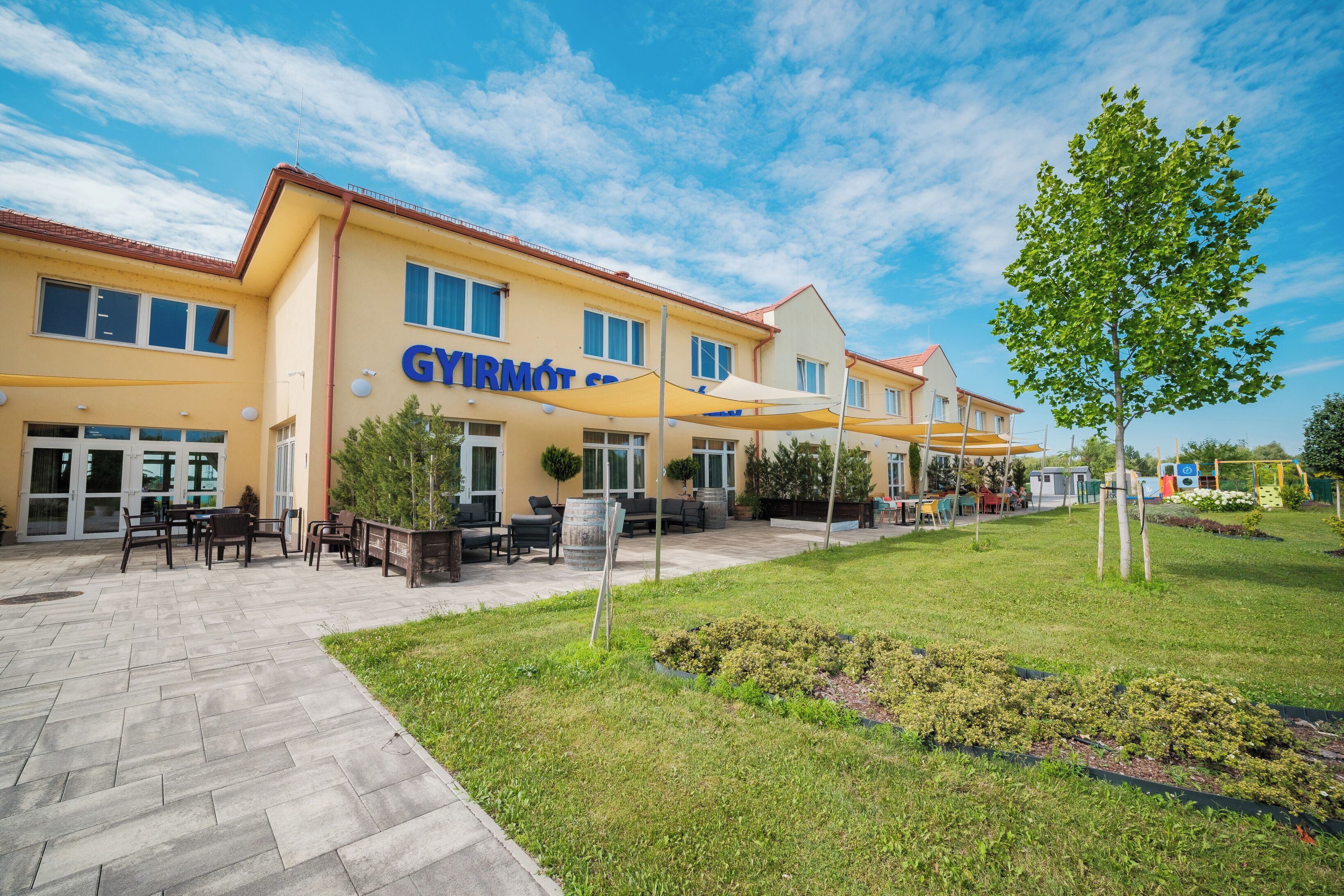 Un bâtiment sur lequel on peut lire l’inscription « GYIRMOT SPA », avec une terrasse aménagée avec des tables et des chaises.