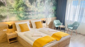 A hotel room with a large bed, wooden headboard, and a mural of a forest scene. There are two chairs and a small table with a bottle. - Gyirmót Sport&Wellness Hotel (Gyor)