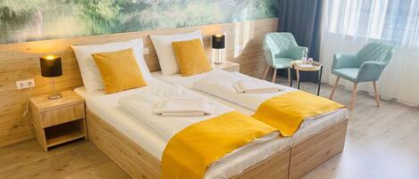 A hotel room with a large bed, wooden headboard, and a mural of a forest scene. There are two chairs and a small table with a bottle.
