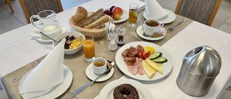 A breakfast table with plates of food, a coffee cup, a juice glass, and a thermos.