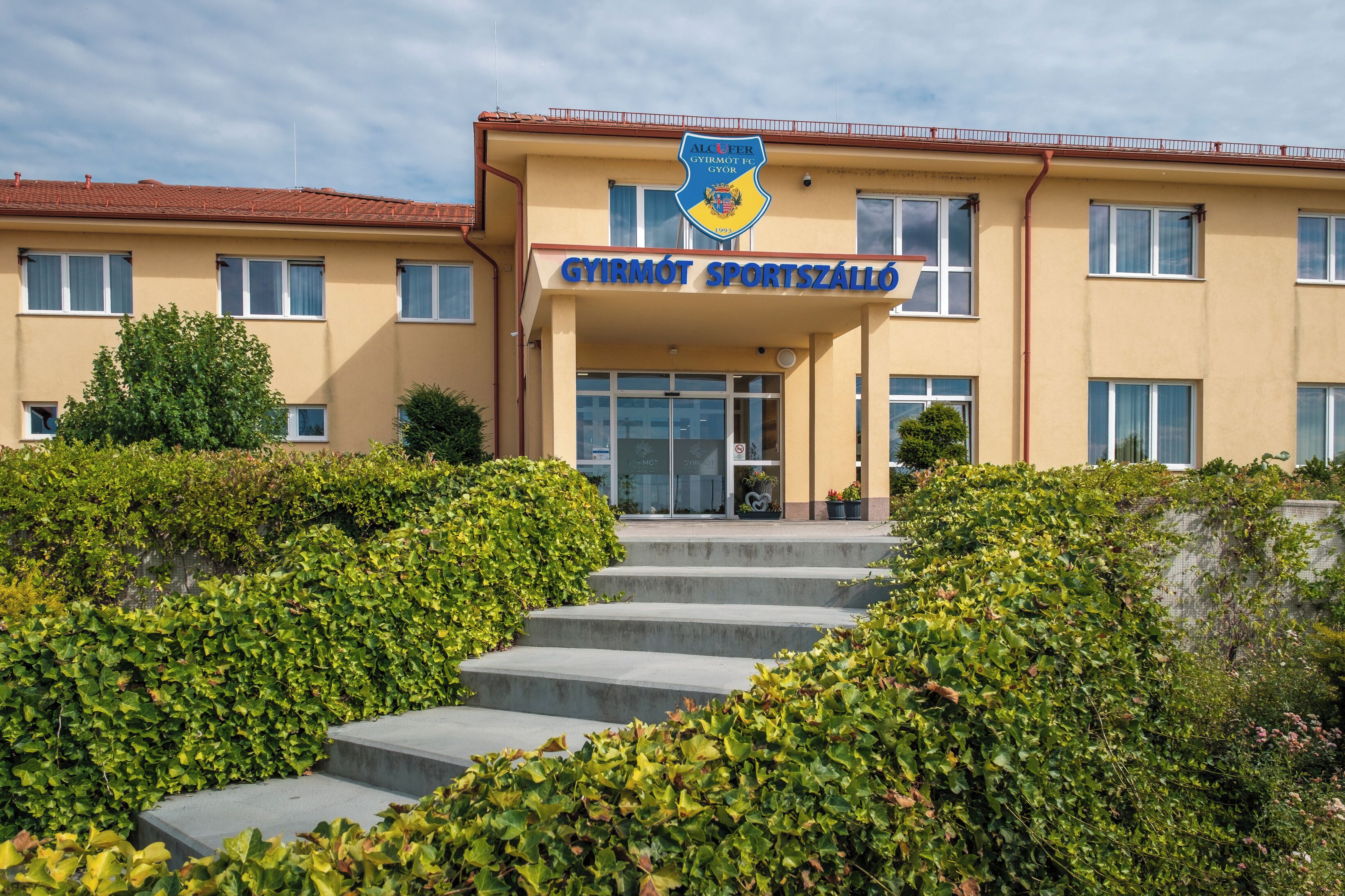 A building with a sign reading 'GYIRMOT SPORTSZÁLLÓ' and a logo above it.