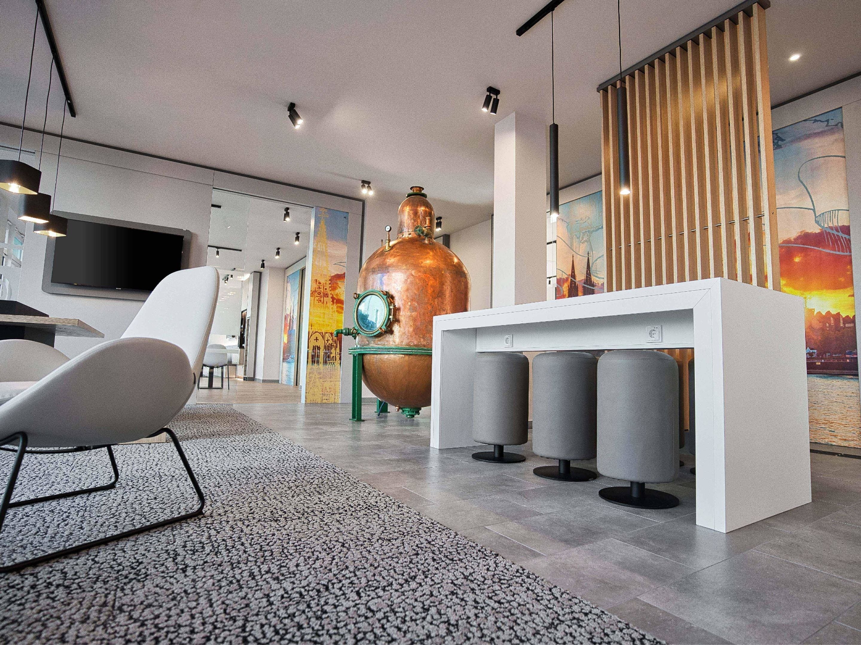 Un interior moderno con un alambique de cobre grande, una mesa blanca con taburetes grises y un televisor de pantalla plana montado en la pared.