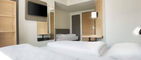 Una habitación de hotel moderna con dos camas, un televisor de pantalla plana montado en la pared y una mesita de noche con lámpara.