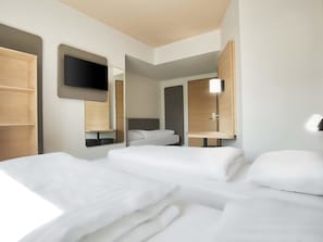 A modern hotel room with two beds, a flat-screen TV mounted on the wall, and a bedside table with a lamp. - B&B Hotel Köln-City (Cologne)