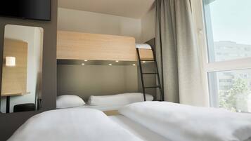 Ein Hotelzimmer mit einem Etagenbett, einem Schreibtisch mit Lampe, einem an der Wand montierten Fernseher und einem Fenster mit Vorhängen.
