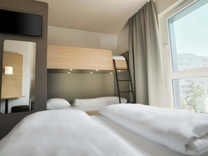 A hotel room with a bunk bed, a desk with a lamp, a TV mounted on the wall, and a window with curtains. - B&B Hotel Köln-City (Cologne)