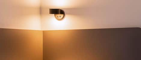 A hotel room with a bed, a wall-mounted light fixture, and a plain wall.