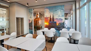 A modern conference room with white tables and chairs, a large mural of a cityscape, and large windows. - B&B Hotel Köln-City (Cologne)
