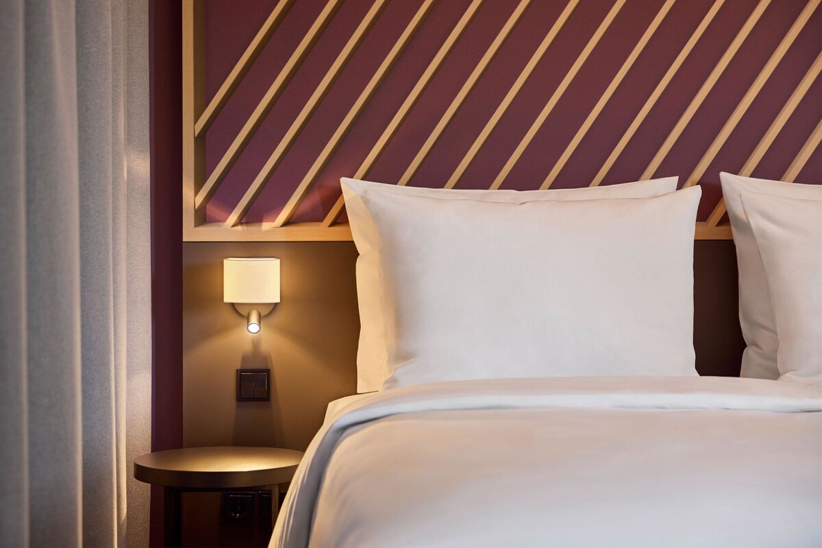 Una camera d'albergo con un letto, un comodino, una lampada a parete e un motivo a righe sul muro.