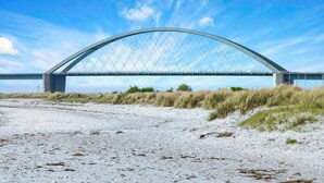 A large, modern bridge with a curved design spanning a sandy area with sparse vegetation. - Landlord Doppelzimmer  22 (Kopendorf auf Fehmarn)