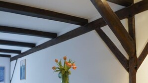 A dining area with a wooden table and two chairs, a vase with flowers on the wall, and exposed wooden beams. - Landlord Doppelzimmer  22 (Kopendorf auf Fehmarn)